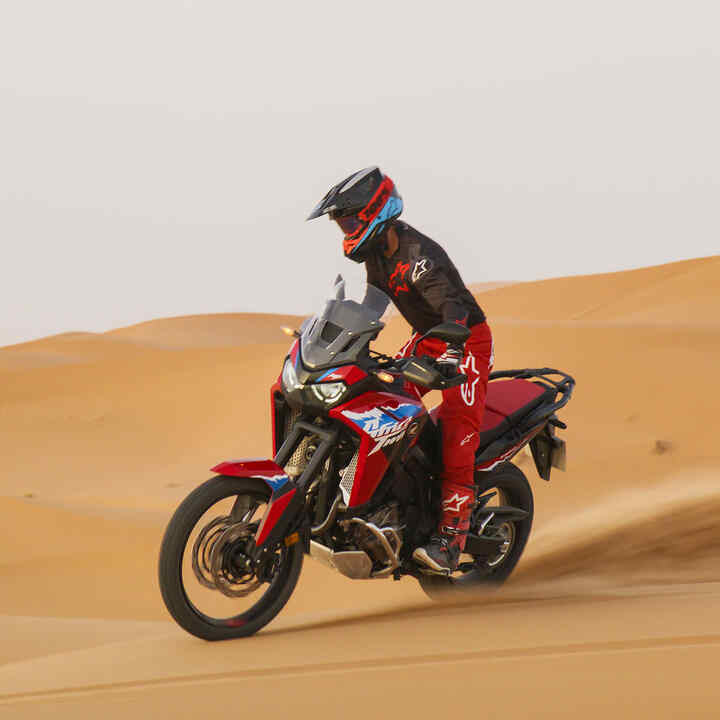 Mannequin conduisant une moto CRF1100L Africa Twin sur une route dans un environnement désertique.