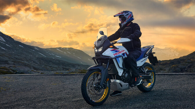 Mannequin conduisant une moto XL750 Transalp sur route en montagne.