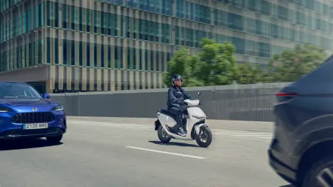 Un motard conduit une moto Honda CUV e dans un endroit urbain.