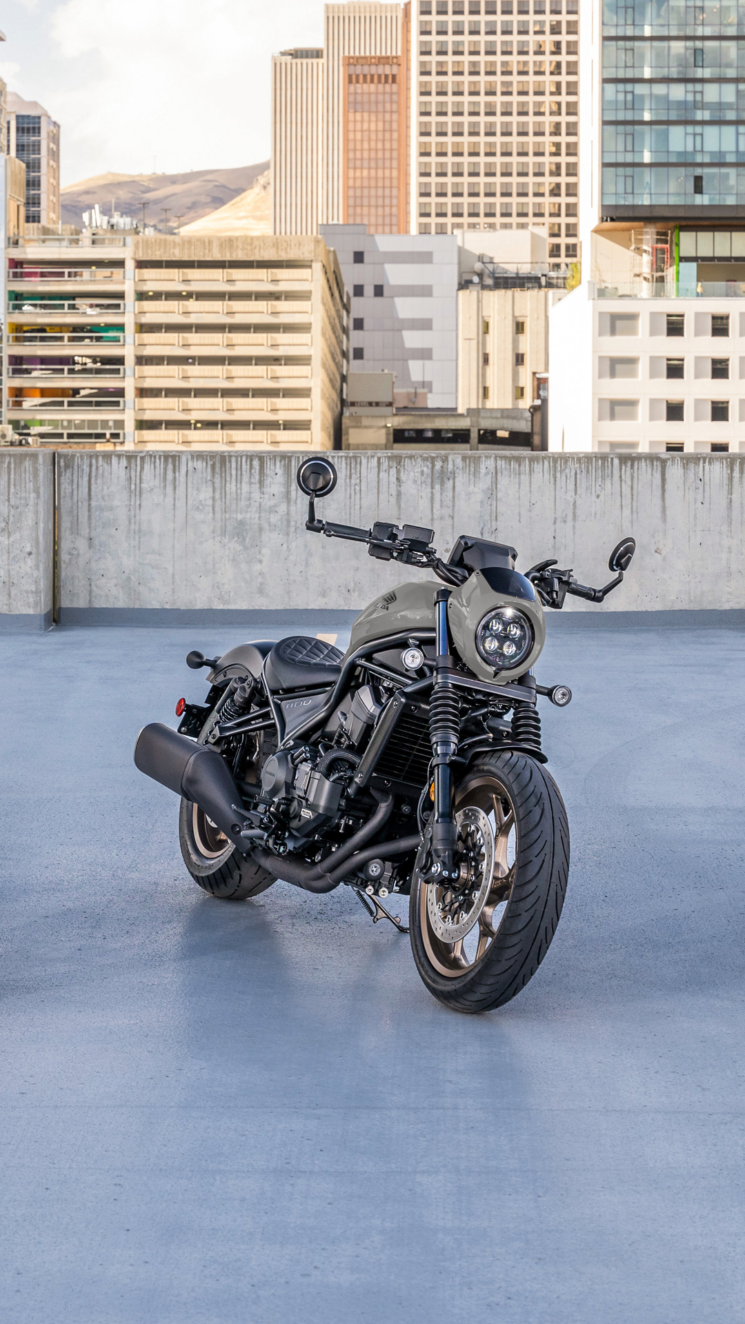 Une moto CMX1100 à l'extérieur, devant un bâtiment moderne.